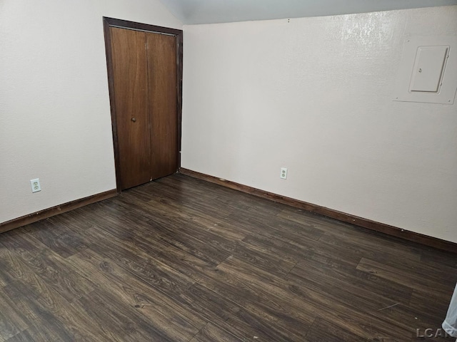 empty room featuring dark wood-type flooring, electric panel, and baseboards