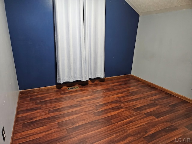 spare room with dark wood-type flooring, visible vents, a textured ceiling, and baseboards