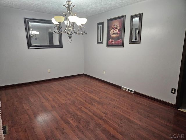 empty room with baseboards, visible vents, dark wood-style flooring, a textured ceiling, and a notable chandelier