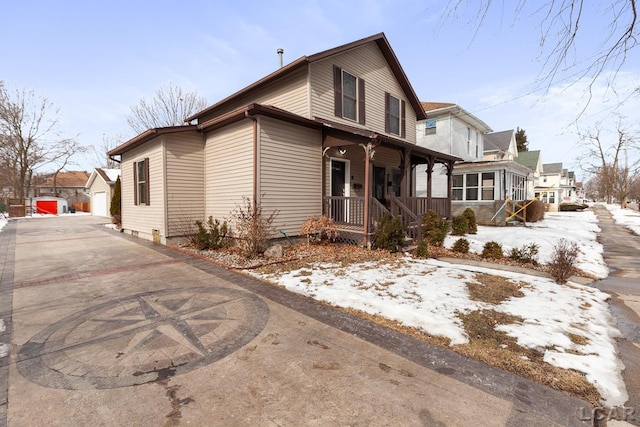 snow covered property featuring a garage, covered porch, and a sunroom