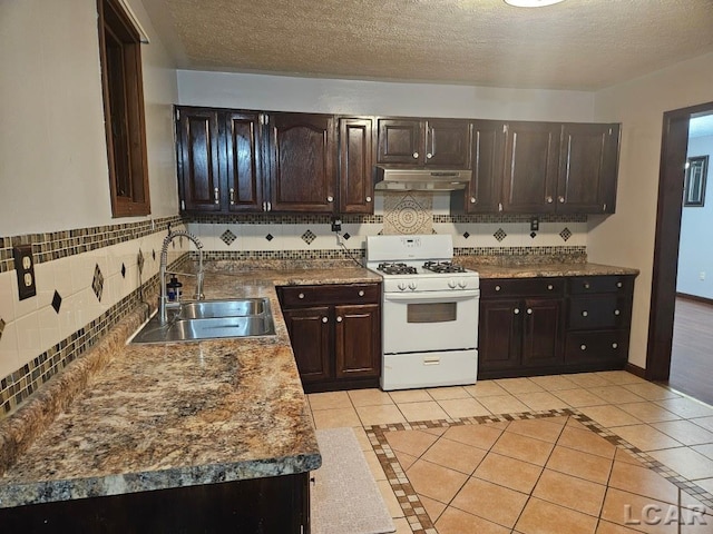 kitchen with light tile patterned floors, white gas range oven, baseboards, under cabinet range hood, and a sink