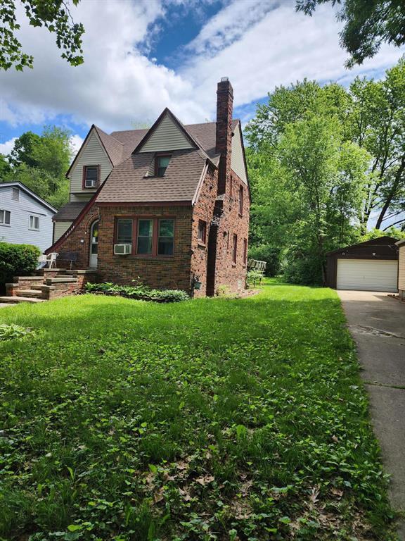 tudor-style house with a detached garage, a chimney, an outdoor structure, a front lawn, and brick siding