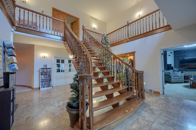 stairway with a high ceiling, marble finish floor, visible vents, and baseboards