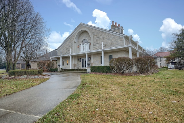 view of front of home with a front yard, stone siding, and a chimney