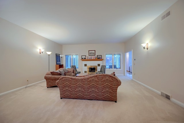 living area featuring baseboards, a fireplace, visible vents, and light colored carpet