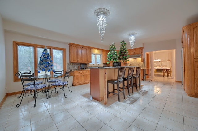 kitchen with light tile patterned floors, tasteful backsplash, a kitchen bar, a kitchen island, and baseboards