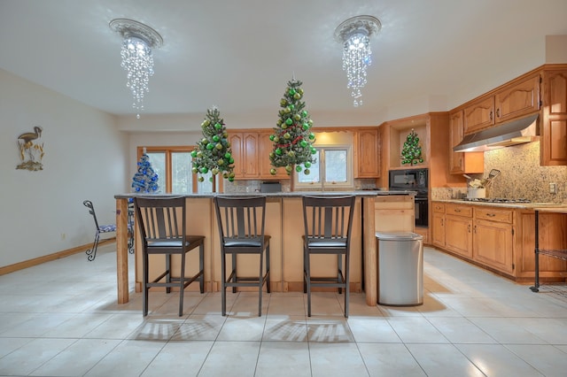 kitchen with a kitchen bar, a center island, under cabinet range hood, and black appliances