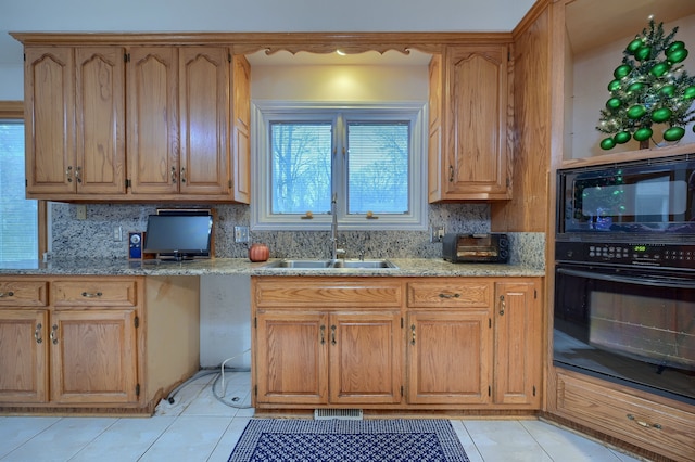 kitchen with light tile patterned floors, decorative backsplash, a sink, light stone countertops, and black appliances