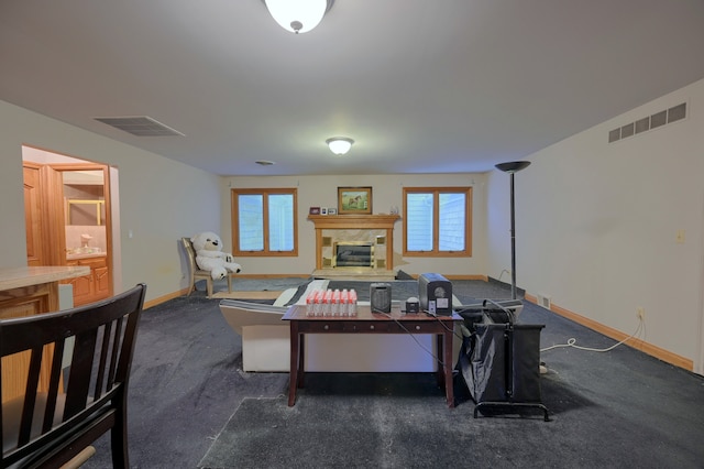 interior space with dark carpet, a glass covered fireplace, visible vents, and baseboards