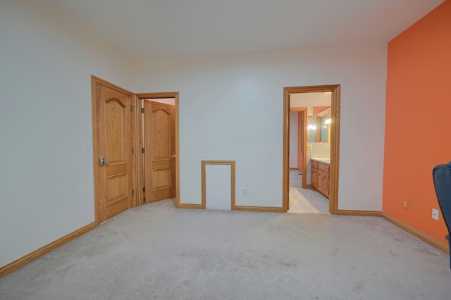 unfurnished bedroom featuring baseboards, ensuite bathroom, and light colored carpet