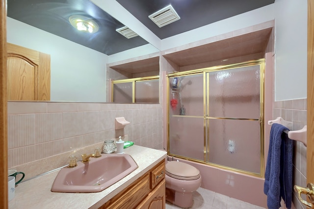 bathroom featuring tile walls, visible vents, toilet, enclosed tub / shower combo, and vanity