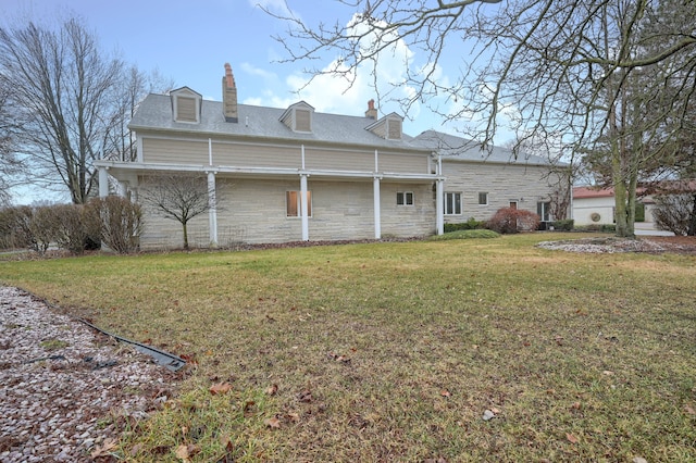 rear view of property featuring stone siding, a lawn, and a chimney