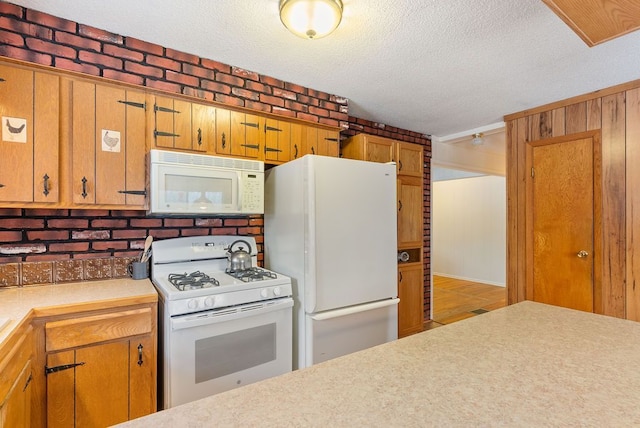 kitchen featuring white appliances, brown cabinetry, brick wall, light countertops, and a textured ceiling