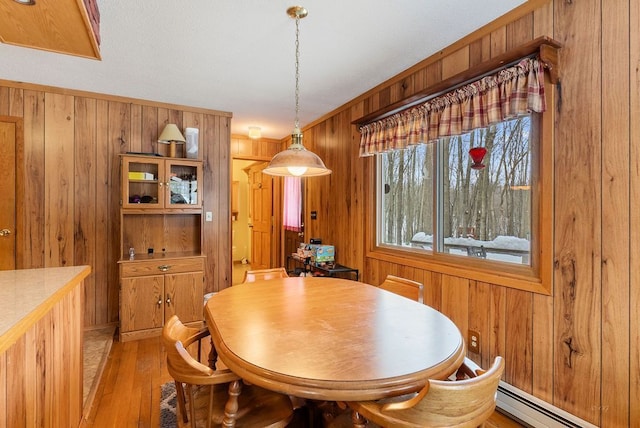 dining space featuring wooden walls, baseboard heating, and light wood finished floors