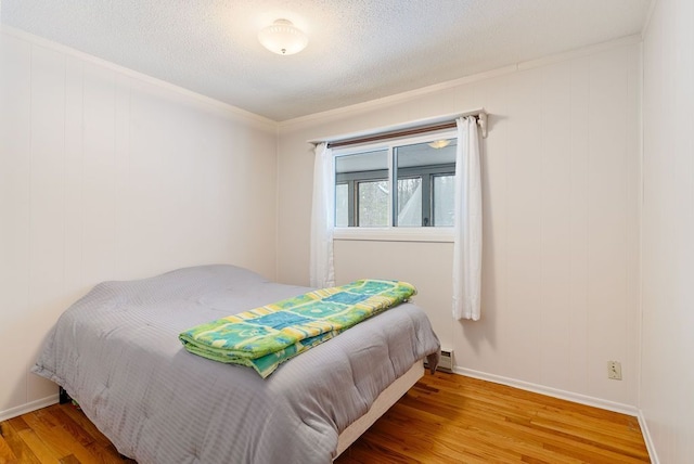 bedroom with a baseboard heating unit, ornamental molding, a textured ceiling, wood finished floors, and baseboards