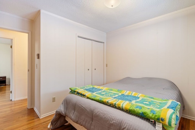 bedroom with a textured ceiling, a closet, wood finished floors, and crown molding