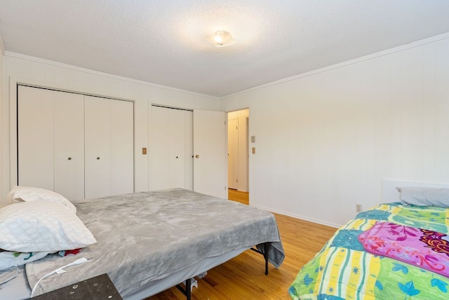 bedroom featuring multiple closets, a textured ceiling, ornamental molding, and wood finished floors