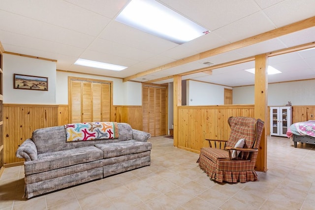 living area with a paneled ceiling, a wainscoted wall, wooden walls, and visible vents