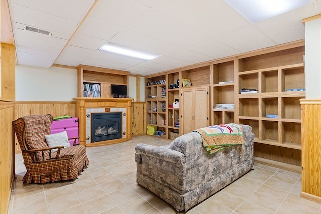 living room with built in features, visible vents, a glass covered fireplace, wainscoting, and a drop ceiling