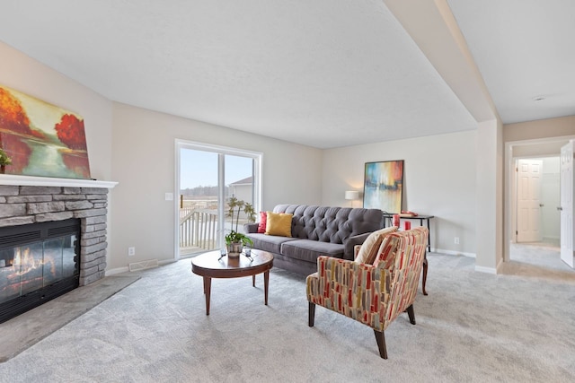 living area featuring visible vents, baseboards, carpet flooring, and a stone fireplace