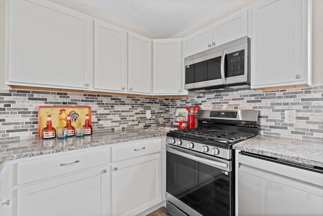 kitchen with white cabinets, light stone countertops, stainless steel appliances, and backsplash