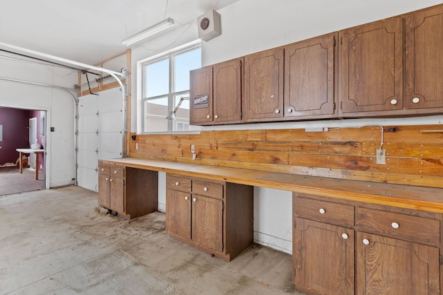 kitchen with brown cabinetry, light countertops, built in study area, and concrete flooring