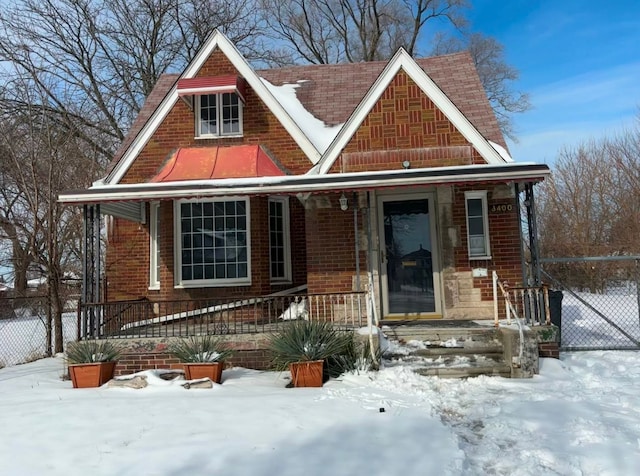 tudor home featuring fence, a porch, and brick siding