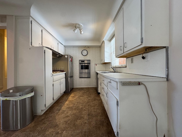 kitchen featuring white cabinets, appliances with stainless steel finishes, light countertops, dark tile patterned floors, and a sink