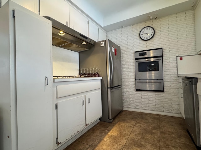 kitchen with a warming drawer, dark tile patterned floors, stainless steel appliances, white cabinetry, and under cabinet range hood