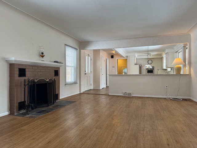 unfurnished living room with visible vents, a fireplace, baseboards, and wood finished floors