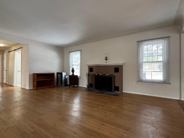 unfurnished living room with a barn door, dark wood-style flooring, a brick fireplace, and baseboards