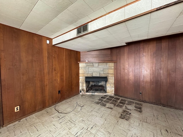 unfurnished living room with a fireplace, visible vents, wood walls, and light floors