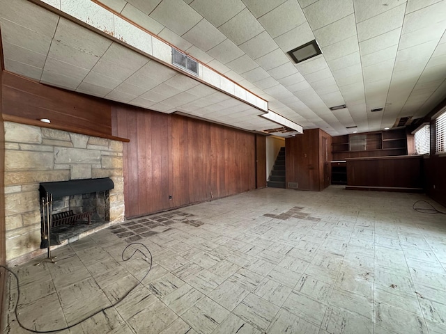 below grade area featuring a stone fireplace, wood walls, visible vents, stairway, and light floors