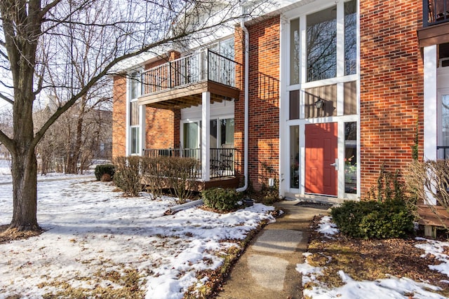 snow covered property entrance featuring brick siding and a balcony