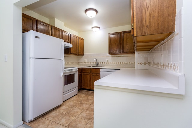 kitchen with white appliances, brown cabinetry, light countertops, under cabinet range hood, and a sink