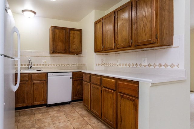 kitchen with light tile patterned floors, light countertops, brown cabinetry, a sink, and white appliances