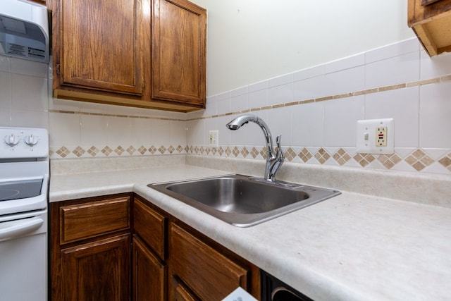 kitchen with brown cabinetry, light countertops, a sink, and electric range