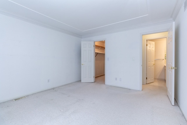 unfurnished bedroom with ornamental molding, light carpet, visible vents, and a spacious closet