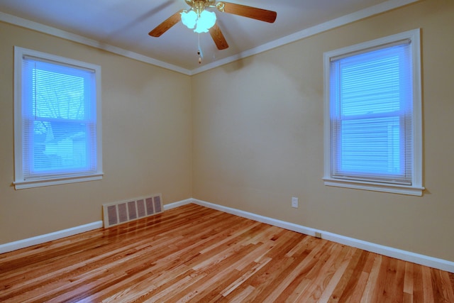 spare room featuring baseboards, visible vents, a ceiling fan, ornamental molding, and light wood-type flooring