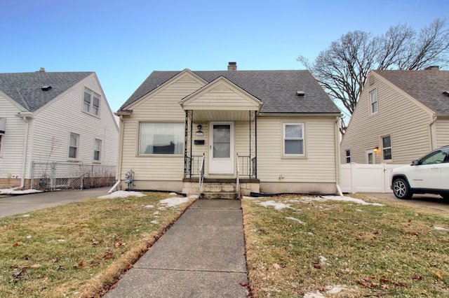 bungalow with a shingled roof, a chimney, fence, and a front lawn