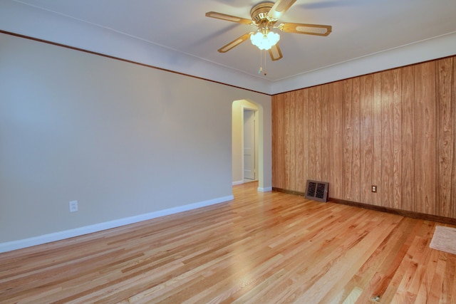 empty room featuring arched walkways, wood finished floors, visible vents, baseboards, and a ceiling fan