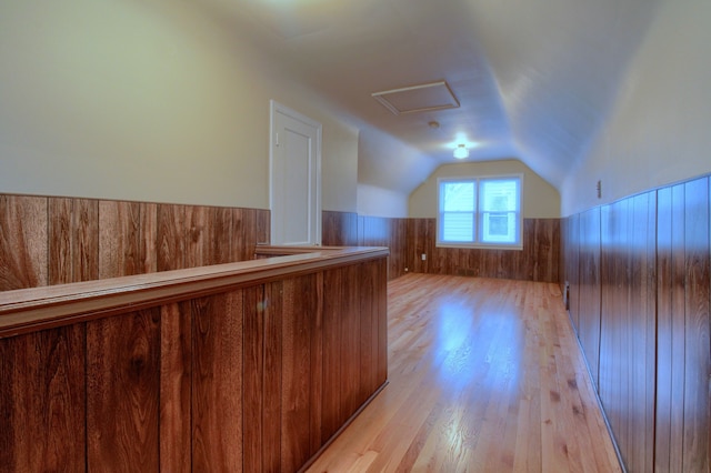 additional living space with attic access, wainscoting, light wood-style flooring, vaulted ceiling, and wood walls