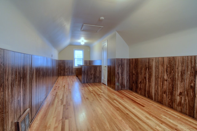 additional living space featuring light wood finished floors, attic access, visible vents, a wainscoted wall, and wood walls