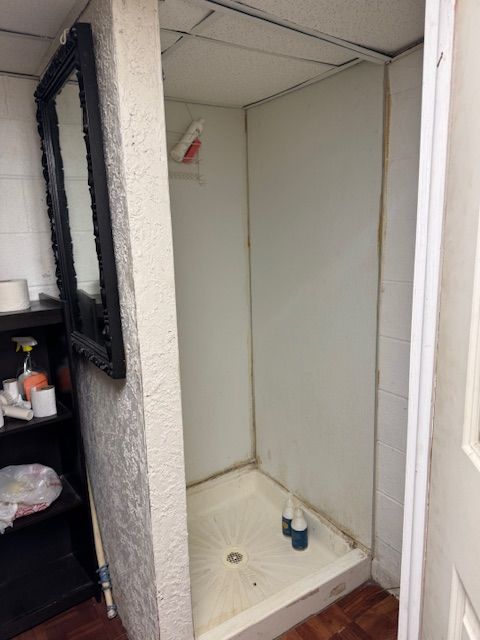 bathroom with a stall shower, a drop ceiling, and concrete block wall