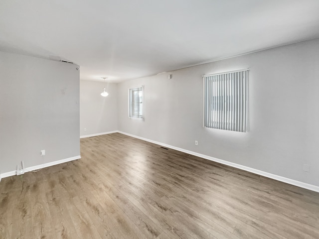 empty room featuring wood finished floors, visible vents, and baseboards