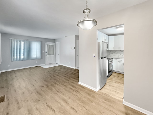 interior space with light wood-type flooring, tasteful backsplash, appliances with stainless steel finishes, and white cabinets