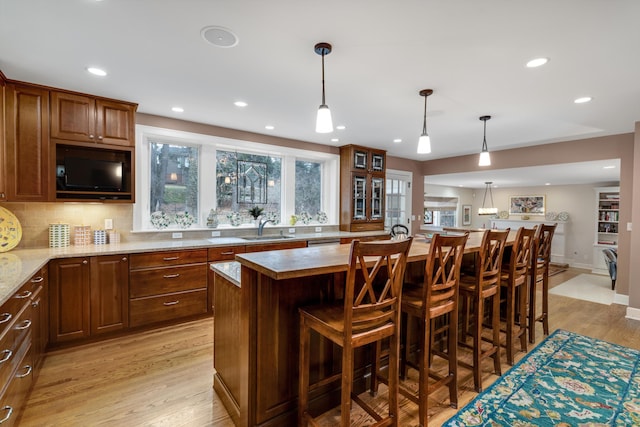 kitchen with a kitchen breakfast bar, a sink, backsplash, and light wood finished floors