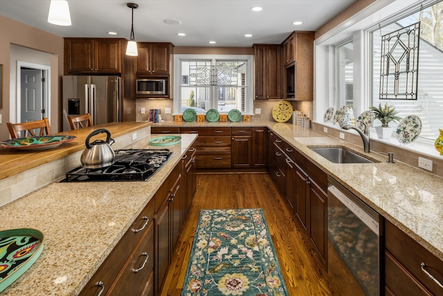 kitchen with light stone counters, stainless steel appliances, dark wood-style flooring, a sink, and decorative backsplash