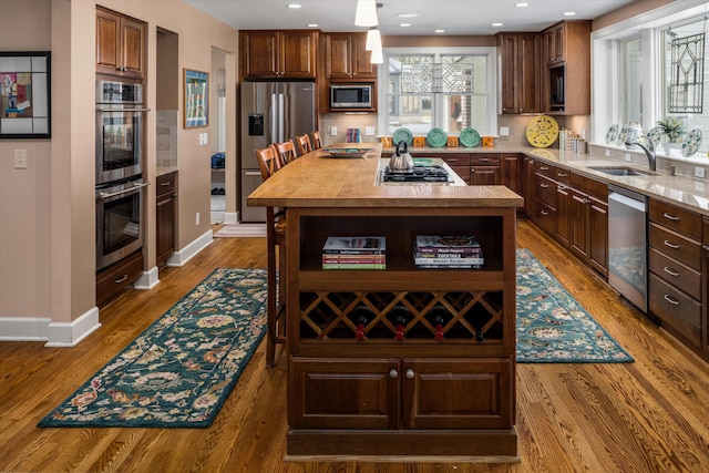 kitchen with baseboards, wood finished floors, a sink, stainless steel appliances, and backsplash