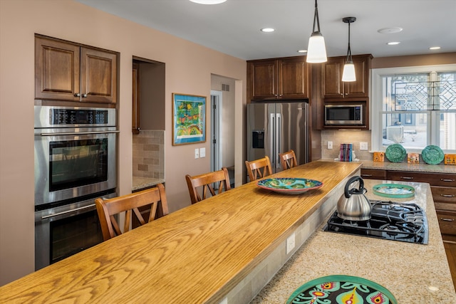 kitchen featuring stainless steel appliances, decorative light fixtures, backsplash, and butcher block countertops